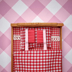 Zwei rosa Zahnbürsten in einem rotkarierten Bett mit passender Gingham-Bettwäsche vor einer rosa karierten Wand.