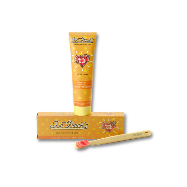 Tube Dr. Bauer's Zahnpasta Active Love Exotic Love 90ml, Schachtel und Bambuszahnbürste mit roten Borsten auf schwarzem Hintergrund - tropische Zahnpflege für ein exotisches Lächeln.