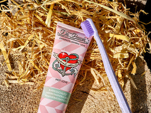 Dr. Bauer’s Zahnpasta Hot Love auf Holzstamm mit Stroh und nachhaltiger Zahnbürste mit lila Borsten