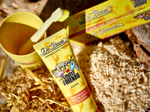 Dr. Bauer’s Zahnpasta ‚Lovely Friends Jungle‘ mit kindlich-verspielten Tiermotiven, umgeben von Holzspänen, Stroh und einem gelben Zahnputzbecher – natürliche Szene mit Fokus auf kinderfreundliche, nachhaltige Zahnpflege.