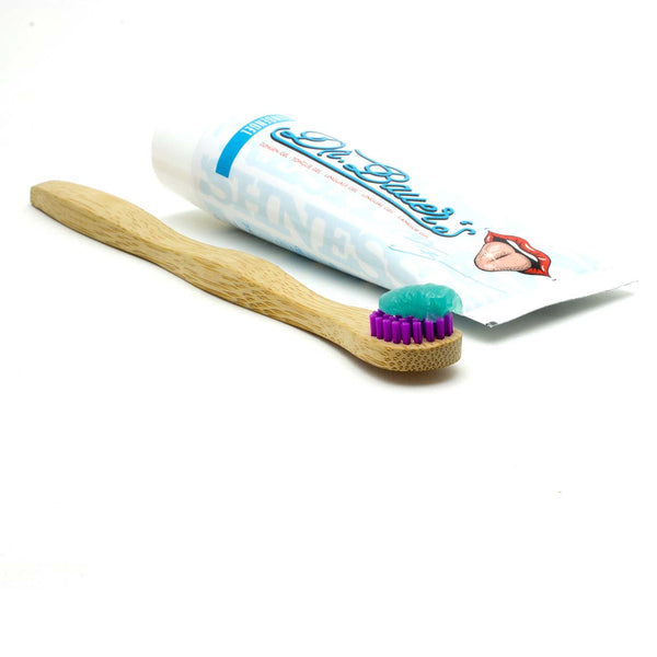 Eine Bambuszahnbürste mit blauer Zahnpasta liegt neben einer Tube Dr. Bauers Zungengel Minze 75ml.