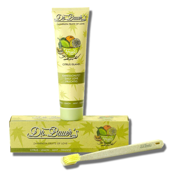 Dr. Bauer's Zahnpasta Fruits of Love Citrus Island 90ml Tube mit natürlichen Inhaltsstoffen, passender Box und einer Zahnbürste mit gelben Borsten vorne.