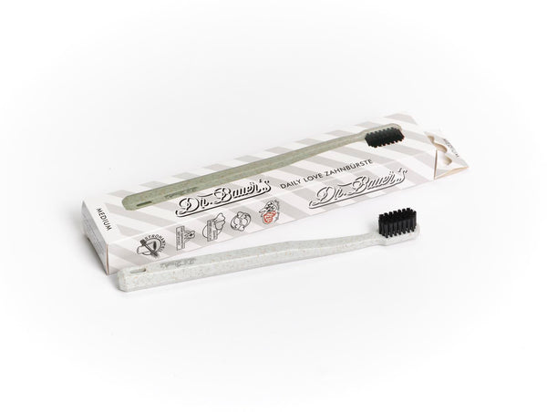 Eine Dr. Bauer's Daily Love Zahnbürste medium mit biobasierten Borsten steht vor ihrer Box, ideal für nachhaltige Zahnpflege.