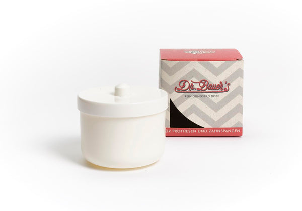 Eine weiße Dr. Bauer's Reinigungsbad-Dose mit Deckel steht neben einer rot-grauen Dr. Bauer's Box, ideal für die Reinigung von Prothesen und Zahnspangen, auf weißem Hintergrund.