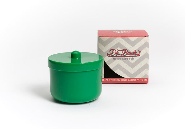 Dr. Bauer's Reinigungsbad-Dose grün mit Deckel neben einer Dr. Bauer's Box auf weißem Hintergrund, perfekt zum Reinigen von Zahnprothesen oder Zahnspangen.