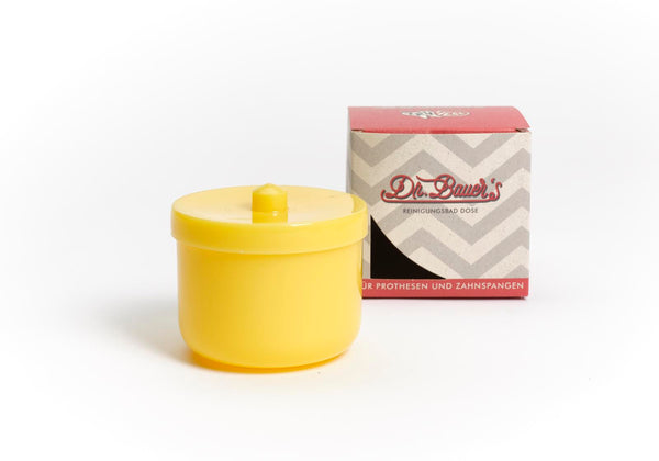 Eine orangefarbene Dr. Bauer's Reinigungsbad-Dose mit Deckel steht neben einer rot-grauen Dr. Bauer's Box, ideal zur Aufbewahrung Ihrer Prothese oder Zahnspange, auf weißem Hintergrund.