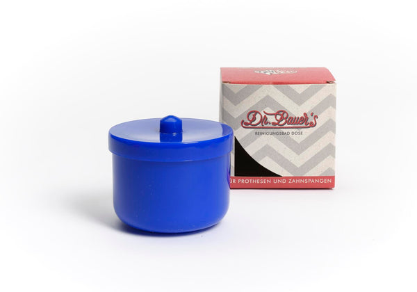 Die Dr. Bauer's Reinigungsbad-Dose blau, ein blauer Kunststoffbehälter mit Deckel zur Reinigung von Zahnprothesen oder Zahnspangen, ist neben einer Schachtel mit dem Markenzeichen von Dr. Bauer auf weißem Hintergrund abgebildet.