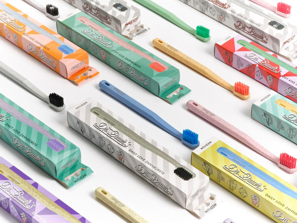 Dr. Bauer‘s Hero Love Whitening Zahnbürsten von Dr. Bauer‘s, mit bunten superweichen Borsten und passenden Boxen, sind ordentlich auf einer weißen Oberfläche angeordnet.