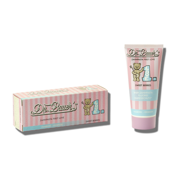 Tube und Dose Dr. Bauer's Zahnpasta First Love Sweet Berries 50ml mit pastellrosa und blauen Streifen, Teddybär, sanftem Schutz und fruchtig-beerigem Geschmack.