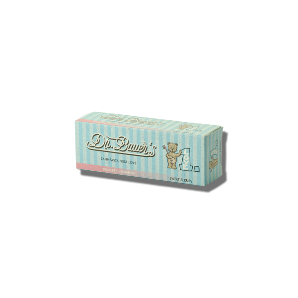 Eine pastellgestreifte Dr. Bauer's Zahnpasta First Love Sweet Berries ohne Fluorid 50-ml-Box mit Teddybär, Flasche und natürlichen Wirkstoffen.