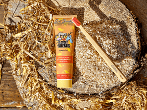 Dr. Bauer’s Zahnpasta ‚Lovely Friends Flamingo‘ mit Holz-Zahnbürste, platziert auf einem Holzstamm mit Spänen und Stroh – fruchtige Kinderzahnpasta mit Glitzer im nachhaltigen Natur-Setting.