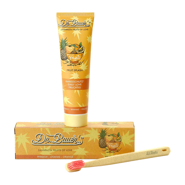 Dr. Bauer's Zahnpasta Fruits of Love Fruit Splash 90ml, im Karton, und einer Bambuszahnbürste mit rosa Borsten auf weißem Untergrund – für sanftes Putzen mit exotischen Fruchtaromen.