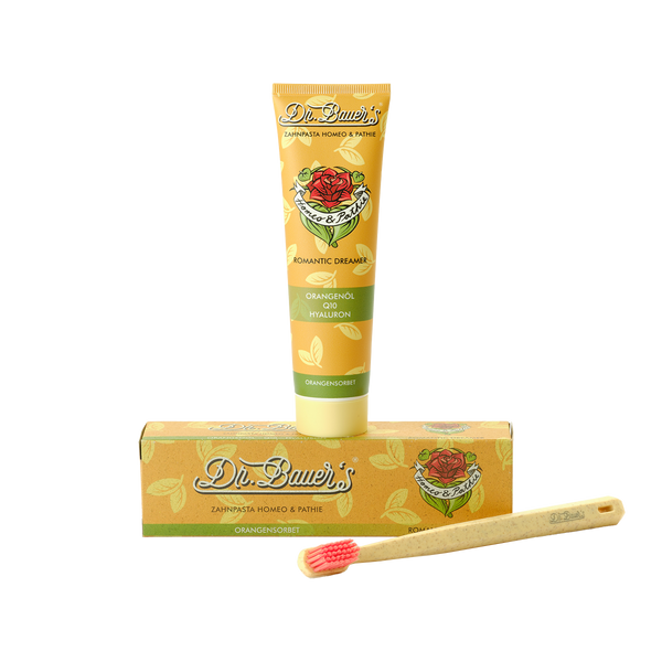 Dr. Bauer's Homöopathie Zahnpasta Romantic Dreamer 90 ml in einer gelben Tube und Schachtel mit einer Bambuszahnbürste auf weißem Hintergrund – eine großartige Wahl für alle, die natürliche Pflege suchen.