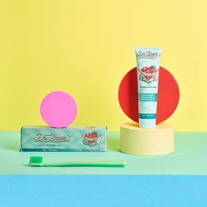 Dr. Bauer’s Zahnpasta ‚Mineral Love – Original Freshness‘ mit Verpackung, grüner Zahnbürste und farbigen Dekoelementen in Pink, Rot und Gelb vor pastellfarbenem Hintergrund – moderne, frische Inszenierung für remineralisierende Zahnpflege mit Meeresmineralien.