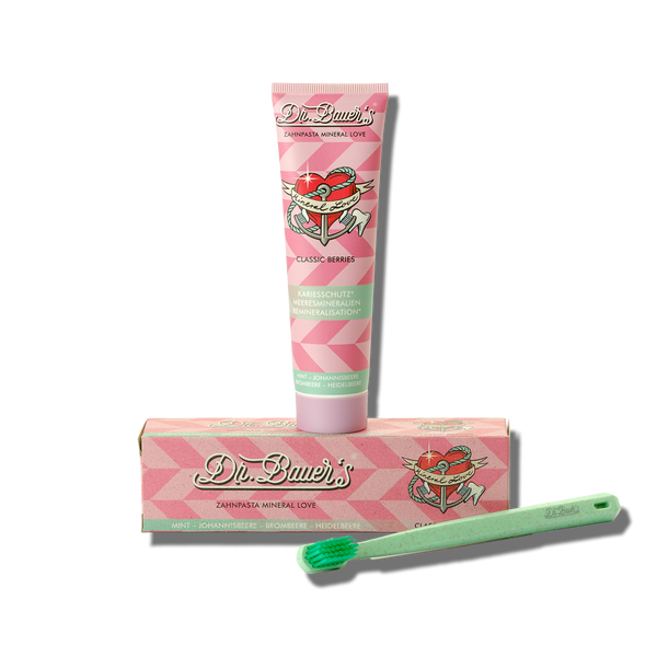 Dr. Bauer's Zahnpasta Mineral Love Classic Berries 90ml in einer rosa Tube mit passender Box und einer grünen Zahnbürste für empfindliche Zähne, abgebildet auf weißem Hintergrund.