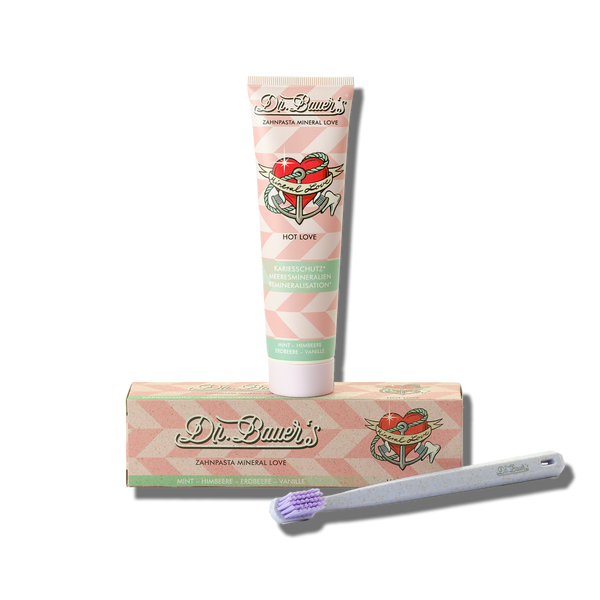 Dr. Bauers Zahnpasta Mineral Love Hot Love 90 ml verleiht Ihrem Alltag zusammen mit der Box und einer weißen Zahnbürste mit violetten Borsten einen Hauch erfrischender Minze.