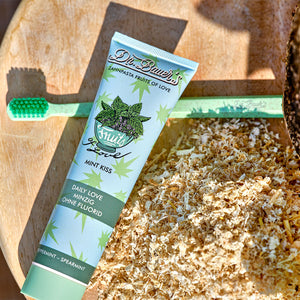 Eine Tube Minzzahnpasta und eine grüne Zahnbürste liegen auf einer Holzoberfläche mit Holzspänen.