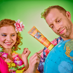 Fröhliche Frau mit Blumenschmuck und Mann mit Hawaiihemd zeigen auf eine Weltkugel, in die eine Dr. Bauer’s Zahnpasta ‚Lovely Friends Flamingo‘ gesteckt ist – bunter, tropisch inspirierter Look mit Urlaubsfeeling.