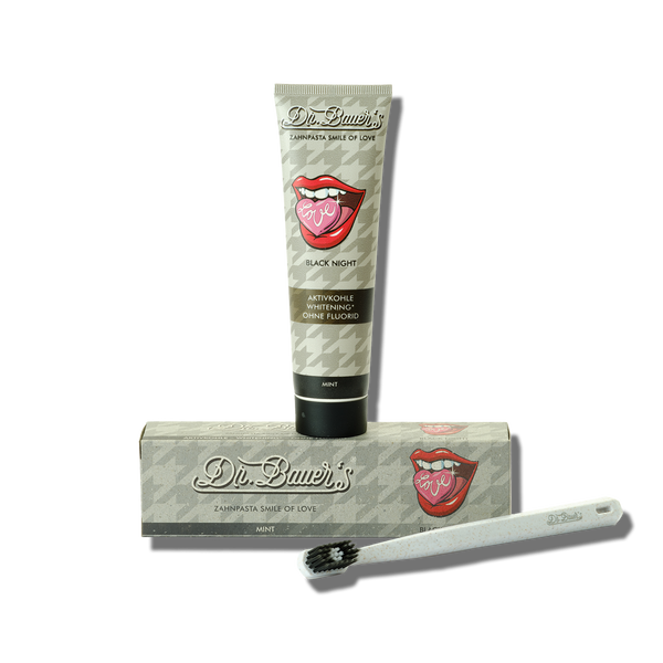 Zur schonenden Reinigung werden Dr. Bauers Zahnpasta Smile of Love Black Night 90ml, eine Zahnbürste und die Produktverpackung vor weißem Hintergrund präsentiert.