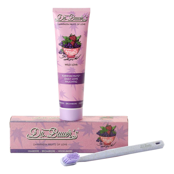 Dr. Bauer's Zahnpasta Fruits of Love Wild Love 90ml und eine violette Zahnbürste sind auf weißem Hintergrund angeordnet und präsentieren natürliche Beerenaromen von Dr. Bauer's für ein geschmackvolles Putzerlebnis.