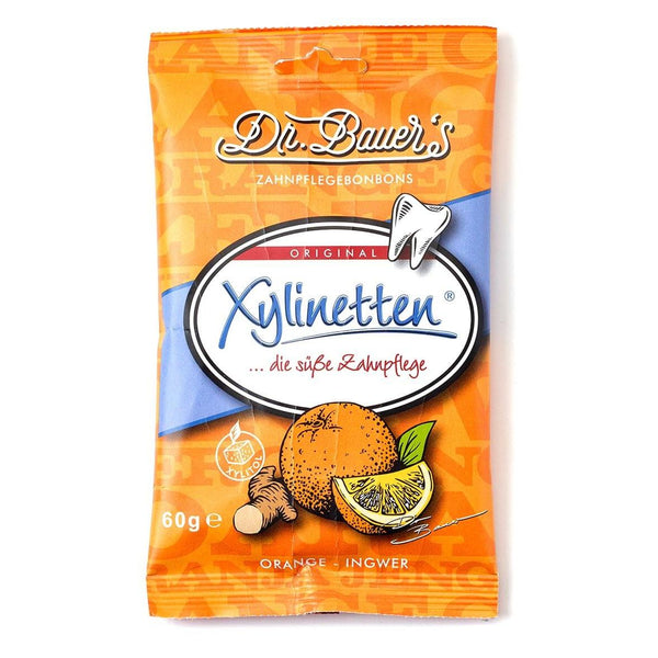 Dr. Bauer’s Xylinetten Orange-Ingwer 60g: Orangen-Weiß-Packung mit Orangen-, Ingwer- und Zahnbildern – ideal für Zahngesundheit und Karies vorbeugen. Marke: Dr. Bauer’s.