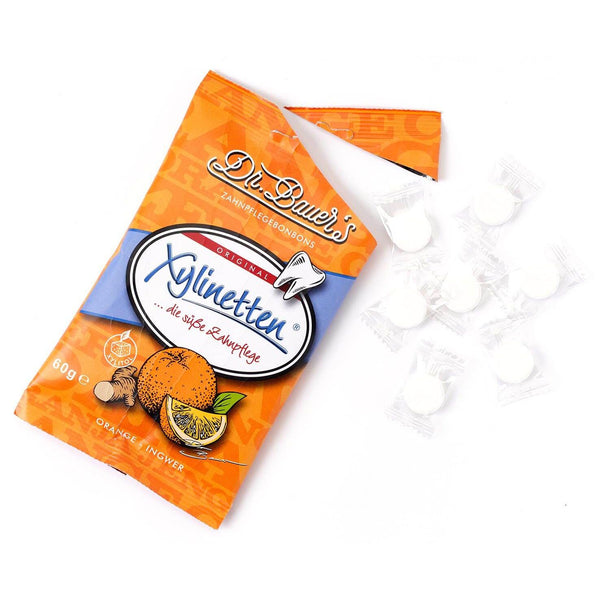 Eine Tüte Dr. Bauer's Xylinetten Orange-Ingwer 60g mit acht einzeln verpackten Bonbons daneben – perfekt für Zahngesundheit und zur Kariesprophylaxe.