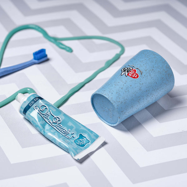 Dr. Bauer's Alpen Fresh Mundpflege-Set von Dr. Bauer's, mit einer blauen Zahnbürste, einer Zahnpastatube und einem gesprenkelten blauen Becher auf einer grau-weißen Oberfläche mit Zickzackmuster.