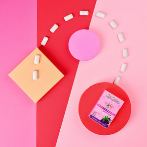 Eine Packung Kaugummi mit weißen Kaugummistücken, die in einem gebogenen Pfad auf einem rosa und roten geometrischen Hintergrund angeordnet sind.