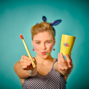 Frau, die eine Zahnbürste und einen Becher in die Kamera hält, mit blauem Hintergrund und unscharfem Gesicht.