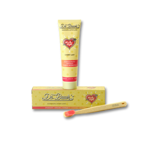 Eine Tube Dr. Bauer's Zahnpasta Active Love Cherry Lady 90ml, die Verpackung und eine Bambuszahnbürste mit roten Borsten sind auf schwarzem Hintergrund arrangiert - und heben die ayurvedische Zahnpflege von Dr. Bauer in der Geschmacksrichtung Kirsche Vanille Spearmint hervor.