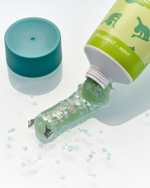 Grünes Minzgel mit Glitter und Tierformen, die aus einer Tube mit grünem Deckel tropfen, mit verstreuten Kristallen.