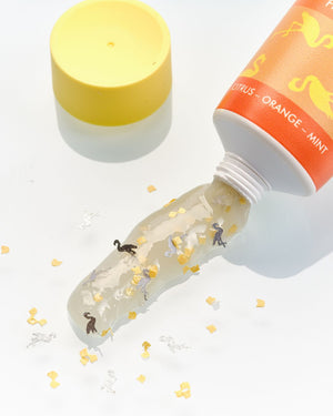 Ein Röhrchen mit klarem Gel und Konfetti-Formen, daneben eine gelbe Kappe, auf weißem Hintergrund.