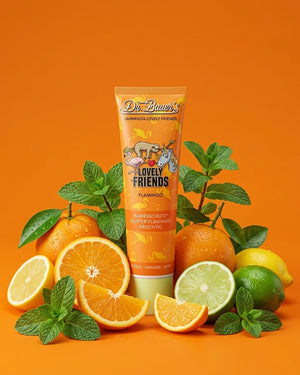 Eine Tube Dr. Bauer's Zahnpasta mit Orangen, Zitronen, Limetten und Minzblättern auf orangem Hintergrund.