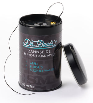 Ein schwarzer Behälter mit Dr. Bauer's ZS-SPENDER Flavor Floss Apple 100m mit abgenommenem Deckel und teilweise herausgezogener Zahnseide.