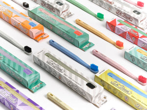 Dr. Bauer‘s Hero Love Whitening Zahnbürsten von Dr. Bauer‘s, mit bunten superweichen Borsten und passenden Boxen, sind ordentlich auf einer weißen Oberfläche angeordnet.