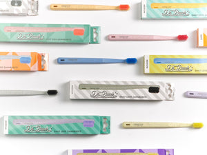 Dr. Bauer‘s Hero Love Whitening Zahnbürsten von Dr. Bauer‘s mit superweichen Borsten und deren Boxen sind flach auf einer weißen Oberfläche angeordnet.