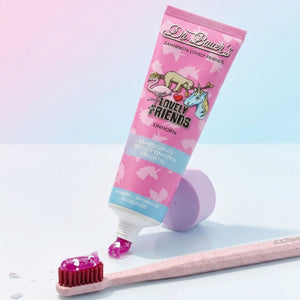 Dr. Bauer's Lovely Friends Einhorn - Kinderzahnpasta mit Glitzer für Kinder ab 6 Jahren, neben einer rosafarbenen Zahnbürste, präsentiert auf pastellfarbenem Hintergrund.
