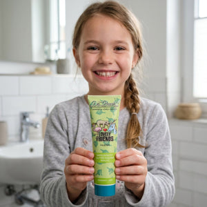 Ein lächelndes junges Mädchen hält in einem Badezimmer eine Tube Dr. Bauer's Zahnpasta Lovely Friends Faultier 90ml Kinderzahnpasta in die Kamera.