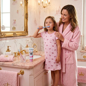 Eine Frau hilft einem kleinen Mädchen beim Zähneputzen mit Dr. Bauer's Zahnpasta Lovely Friends Prinzessin 90ml in einem rosafarbenen, prinzessinnenhaften Badezimmer, das mit verspielten Abziehbildern und Zitaten in Helvetica Neue an den Wänden dekoriert ist.