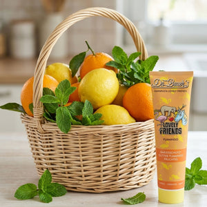 Ein Korb mit Zitronen, Orangen und Minze steht neben der Flamingo Zahnpasta Kinder - Lovely Friends (90 ml) von Dr. Bauer, einer Kinderzahnpasta mit Zitrusgeschmack und Xylit für sicht- und schmeckbare Frische.