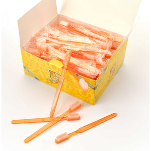 Eine gelbe Schachtel von Dr. Bauer's Einmalzahnbürsten mit Zahnpasta 100er Packung ORANGE, mit einzeln verpackten orangefarbenen Zahnbürsten im Inneren und ein paar außen ausgestellten Zahnbürsten.