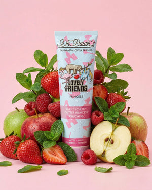 Eine Tube Dr. Bauers Zahnpasta, umgeben von Äpfeln, Erdbeeren, Himbeeren und Minzblättern auf einem rosa Hintergrund.