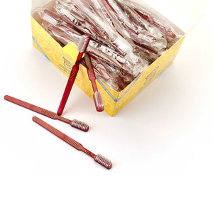 Eine gelbe Schachtel mit Dr. Bauers Einmalzahnbürsten mit Zahnpasta 100er Packung ROT, mit einzeln verpackten roten Zahnbürsten und einigen unverpackten neben der Schachtel.