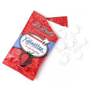 Daneben ist eine rote Tüte Dr. Bauer’s Xylinetten Erdbeere 60g mit sieben unverpackten weißen Bonbons abgebildet.
