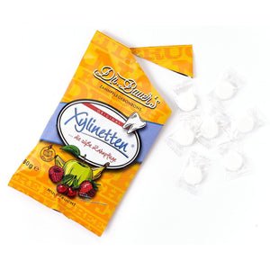 Eine geöffnete Dr. Bauer's Xylinetten Multi Frucht 60g Tüte mit mehreren einzeln verpackten Bonbons aus natürlichem Xylitol daneben.