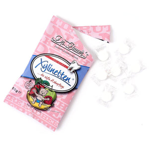 Dr. Bauer‘s Xylinetten Tutti Frutti 60g Beutel in Pink, daneben verstreut mehrere einzeln verpackte weiße Dr. Bauer‘s Bonbons.