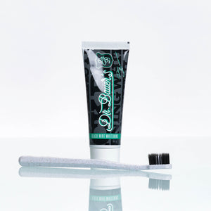 Hinter einer weißen Zahnbürste mit schwarzen Borsten steht eine Tube des Hero Love Whitening Sets von Dr. Bauer.