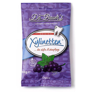 Dr. Bauer's Xylinetten Cassis 60g wird in einem violetten Beutel mit einer schwarzen Johannisbeere-Illustration und einem Zahnsymbol geliefert, das auf Zahnpflege hinweist.